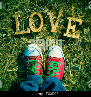 Primo piano dei piedi di un uomo che indossa red sneakers stepping sul prato dove un mucchio di lettere in legno formano la parola amore, con Foto Stock