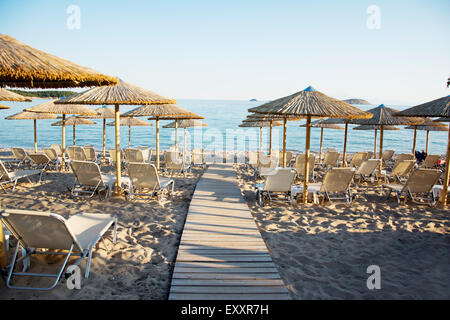 E sabbiosa spiaggia di ciottoli con sedie a sdraio e ombrelloni al tramonto Foto Stock