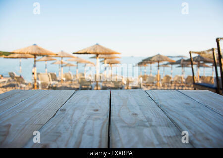 Tavolo in legno con spiaggia con lettini e ombrelloni al tramonto in background Foto Stock