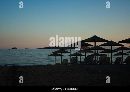 E sabbiosa spiaggia di ghiaia con lettini e ombrelloni al tramonto Foto Stock