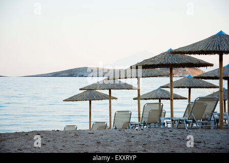 E sabbiosa spiaggia di ciottoli con sedie a sdraio e ombrelloni al tramonto Foto Stock