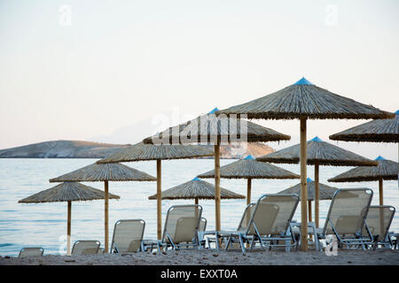 E sabbiosa spiaggia di ciottoli con sedie a sdraio e ombrelloni al tramonto Foto Stock