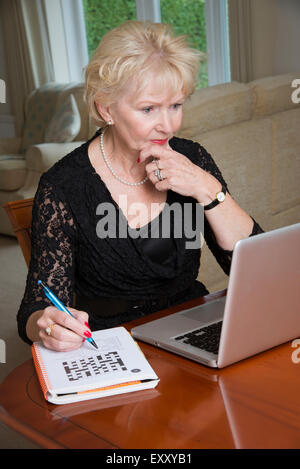 Donna anziana completando un cruciverba utilizzando il computer portatile Foto Stock