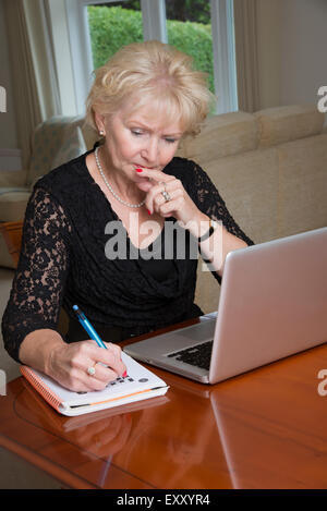 Donna anziana completando un cruciverba utilizzando il computer portatile Foto Stock