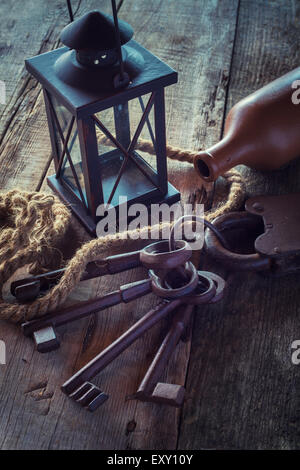 Vecchio arrugginito serratura con chiavi, lampada vintage, bottiglia da argilla e fune su tavola di legno. Retrò foto stilizzata. Foto Stock