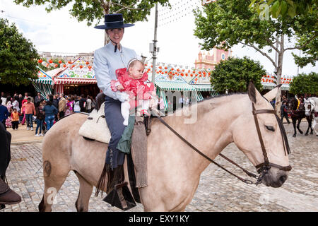 Cavaliere a cavallo nel tradizionale abito di Siviglia con un bambino essendo mantenuto per buona fortuna per il bambino a Siviglia, in Andalusia, Spagna, Europa Foto Stock