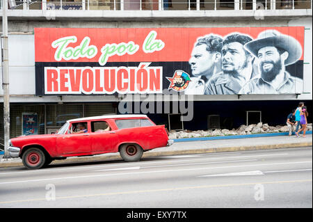 L'Avana, Cuba - Giugno 2011: Billboard promozione di propaganda comunista si erge sopra vintage americano auto passando sotto il la rampa. Foto Stock