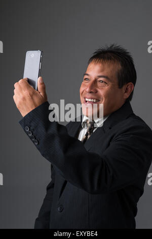 Un imprenditore ispanica azienda tenendo un selfie con il suo telefono cellulare. Foto Stock