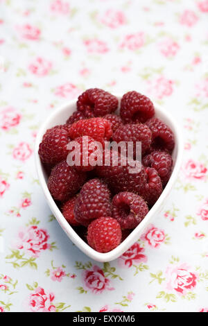 Rubus idaeus 'autunno Bliss". Appena raccolto i frutti a bacca rossa in una ciotola panno floreali. Foto Stock