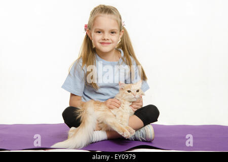 6 anno vecchia ragazza europei dopo esercizio seduti su un tappeto con un gatto domestico Foto Stock