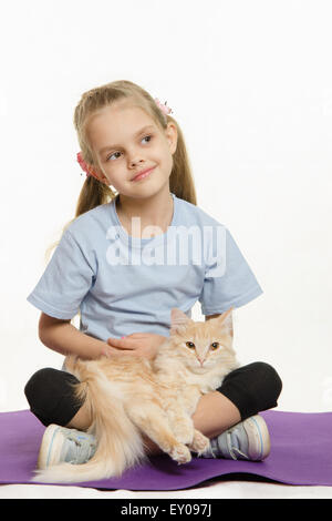 6 anno vecchia ragazza europei dopo esercizio seduti su un tappeto con un gatto domestico Foto Stock