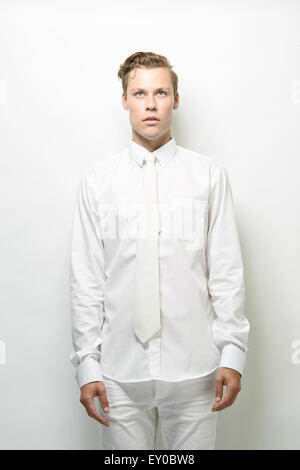 Una bionda, uomo bello, modello maschile, in piedi indossando un vestito bianco, guardando verso l'alto. Un futuristico concetto di moda. Foto Stock