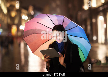 Donna con imbottitura sotto ombrellone nella città di sera Foto Stock