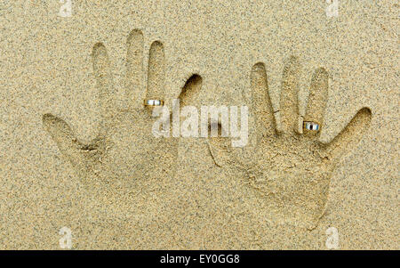 Due forme di mano nella sabbia. Ogni mano ha un dorato anello nuziale al quarto dito. Foto Stock