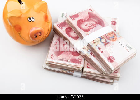 Il cinese 100 RMB banconote impilate, con un felice salvadanaio nella parte superiore sinistra dell'immagine. Foto Stock