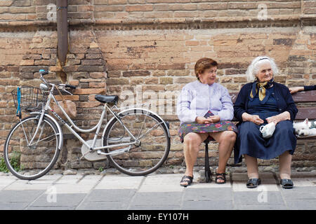 Due anziane signore seduto su una panchina accanto a una bicicletta di fronte a un muro di mattoni. Foto Stock