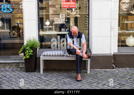 Senior anziano uomo seduto su un banco di lavoro al di fuori del negozio e regolazione della calzatura Foto Stock