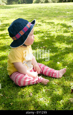 Vista laterale di una bambina guarda pensieroso seduto sull'erba Foto Stock