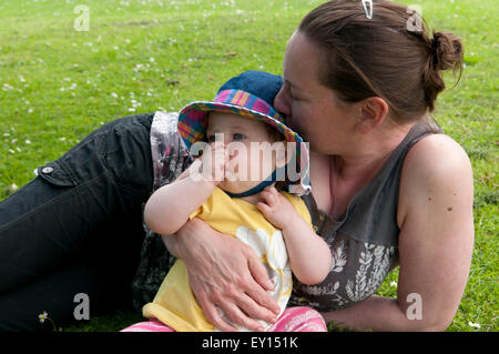 Baby girl succhiare il suo pollice e di essere confortati da sua madre nel giardino Foto Stock