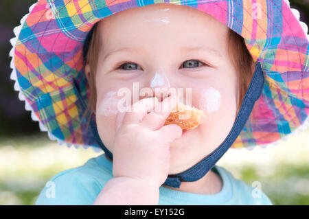 Ritratto di una bambina indossa un cappello per il sole di mangiare il pane con crema solare sul suo viso Foto Stock