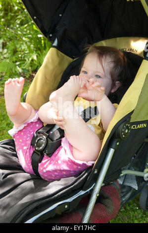 Baby girl nel suo passeggino all'aperto a giocare con i suoi piedi Foto Stock