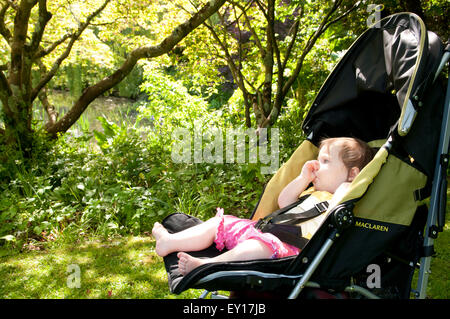 Baby girl nel suo passeggino all'aperto succhiare il suo pollice Foto Stock