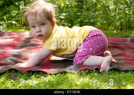 Ritratto di una bambina all'aperto cercando di strisciare, guardando la telecamera Foto Stock