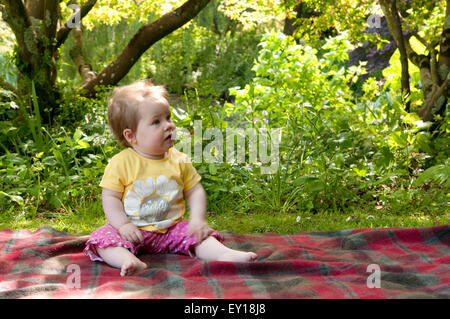 Baby girl nudo seduto su un tappeto all'aperto Foto Stock