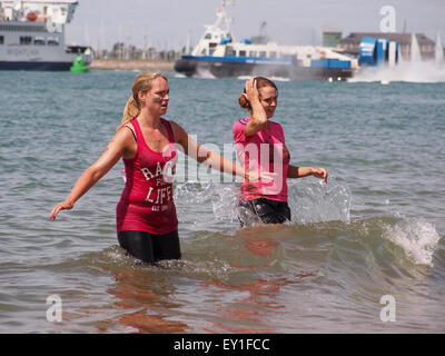 Due signore raffreddare e lavare il fango da loro la pelle in mare dopo la bella gara di fango per la vita a Southsea Foto Stock