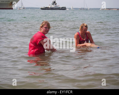 Due signore raffreddare e lavare il fango da loro la pelle in mare dopo la bella gara di fango per la vita a Southsea Foto Stock