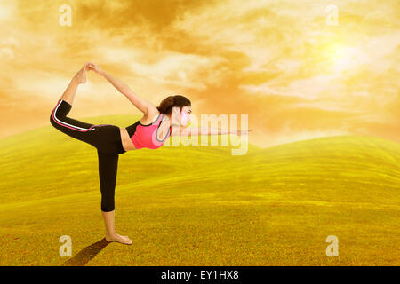 Giovane donna facendo esercizio di yoga su erba con il cielo al tramonto Foto Stock