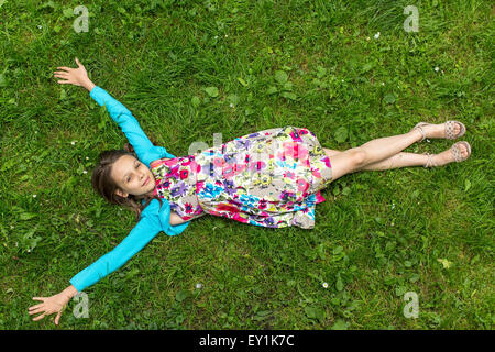 Carino bambina sdraiati sull'erba, braccia tese, vista dall'alto. Foto Stock