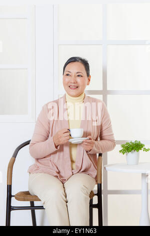 Senior donna tenendo una tazza di bevanda e guardando lontano con sorriso, Foto Stock