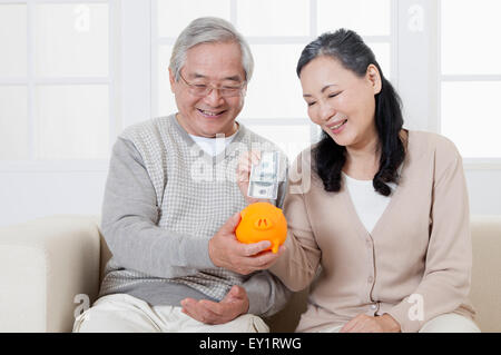 Coppia senior mettendo la carta moneta nel salvadanaio con sorriso, Foto Stock