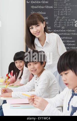 Giovane insegnante insegnamento agli studenti in classe e sorridente alla telecamera, Foto Stock