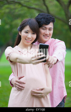 Giovane uomo e donna incinta guardando il telefono cellulare e scattare foto con sorriso, Foto Stock