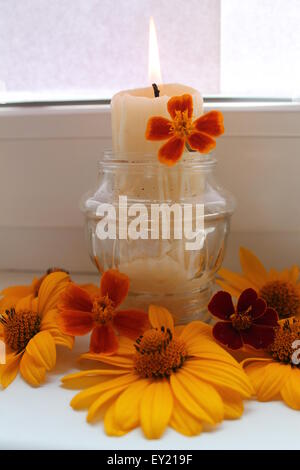 Masterizzare white candela in vaso di vetro decorate con fiori arancione Foto Stock