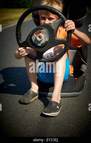 Driver. Gara immaginaria. Ragazzo bambino immaginario di guida auto sulla strada trattenendo il volante Foto Stock