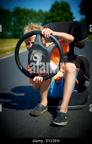 Driver. Gara immaginaria. Ragazzo bambino immaginario di guida auto sulla strada trattenendo il volante Foto Stock