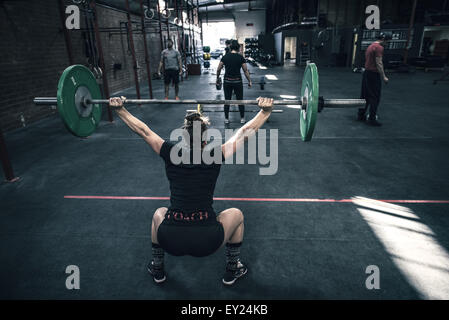 Vista posteriore del giovane donna accovacciata con barbell in palestra Foto Stock