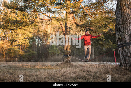 Giovane uomo bilanciamento sulla slackline in foresta Foto Stock