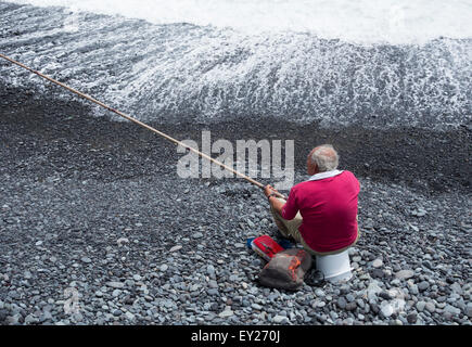 Uomo anziano pesca dalla spiaggia rocciosa Foto Stock