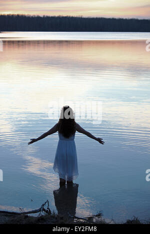 Una ragazza in un abito bianco in acque poco profonde al crepuscolo Foto Stock
