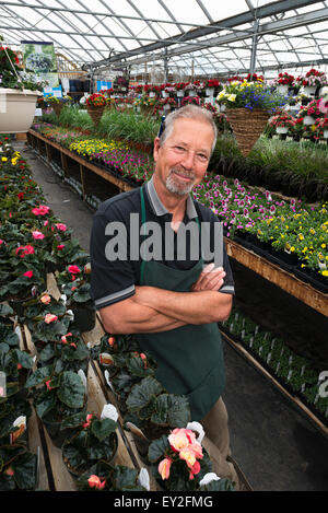 Un uomo in piedi in una serra con ripiani di piante. Foto Stock