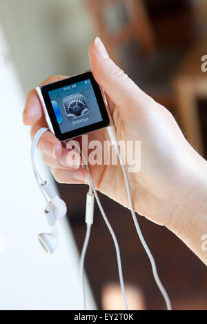 Close up di un Apple iPod nano con cuffie, tenuto in una mano di donna che mostra la schermata delle impostazioni. Foto Stock