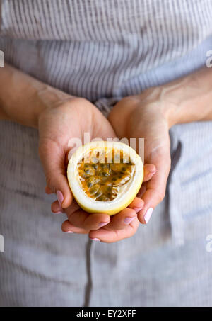 Una donna che mantiene la metà di un taglio fresco il frutto della passione nelle sue mani. Foto Stock