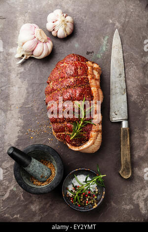 Materie roast beef scamone, condimenti e il coltello sulla pietra scura sullo sfondo di ardesia Foto Stock
