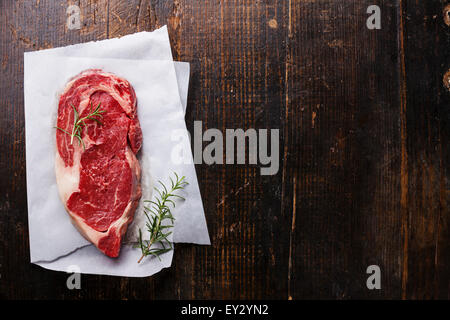Crudo fresco di carne in marmo nero bistecca angus e rosmarino scuro dello sfondo in legno Foto Stock