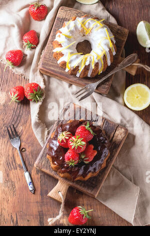 In casa torte al cioccolato con fragole e cioccolato fondente ganache e glassa bianca e la scorza di limone, servita in piccole casette di legno Foto Stock