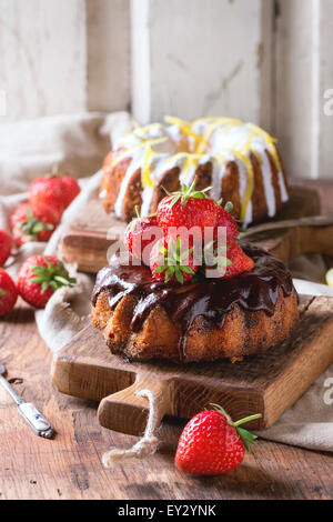 In casa torte al cioccolato con fragole e cioccolato fondente ganache e glassa bianca e la scorza di limone, servita in piccole casette di legno Foto Stock